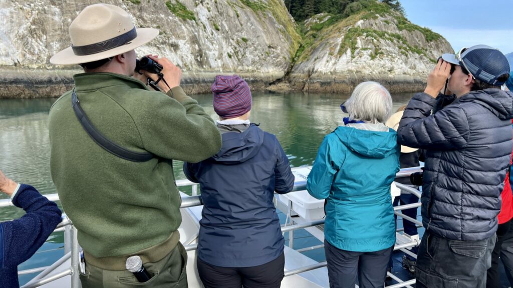 A Park Ranger with binoculars looking for birds to call out to the passengers on the boat tour he is leading. 