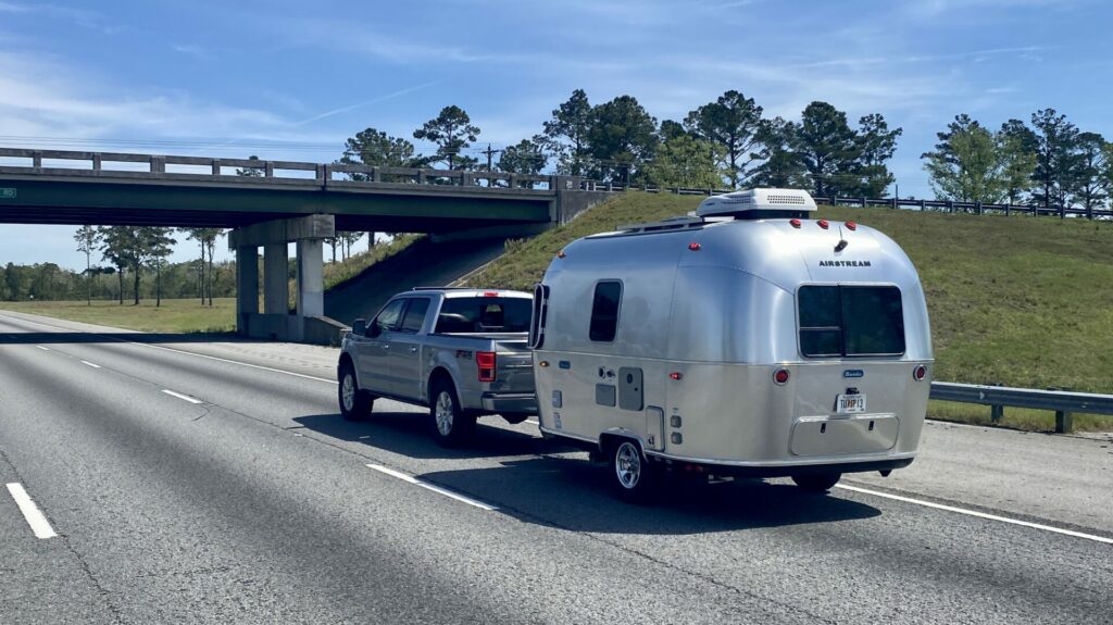 A truck towing a small Airstream travel trailer down the freeway.