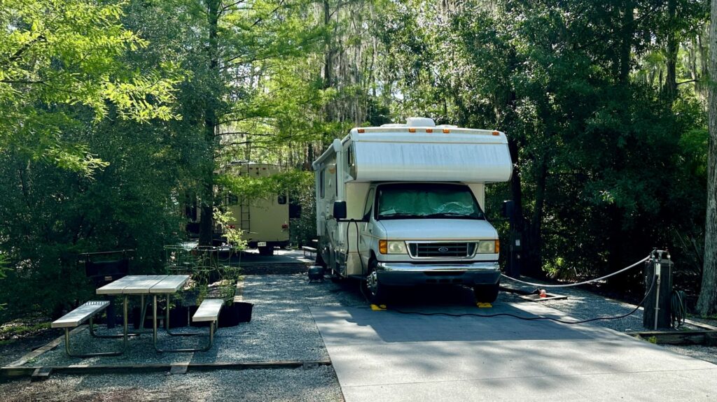 A Class C motorhome parked in a campground with a picnic table. 