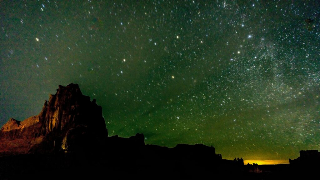 A location in the southwest at night with rock formations and a dark greenish sky with stars.
