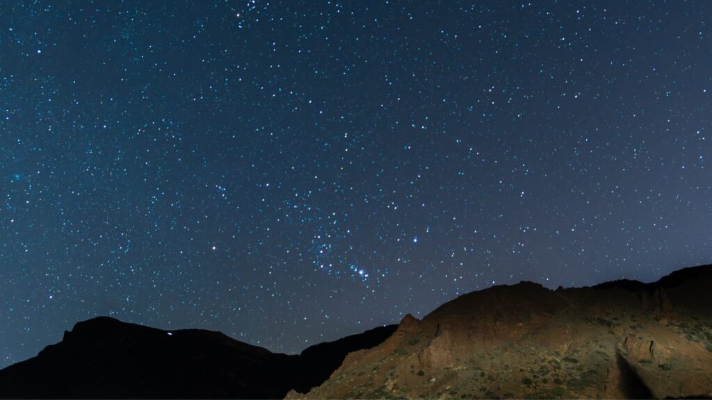 A night sky with stars and rocks in the foreground. 