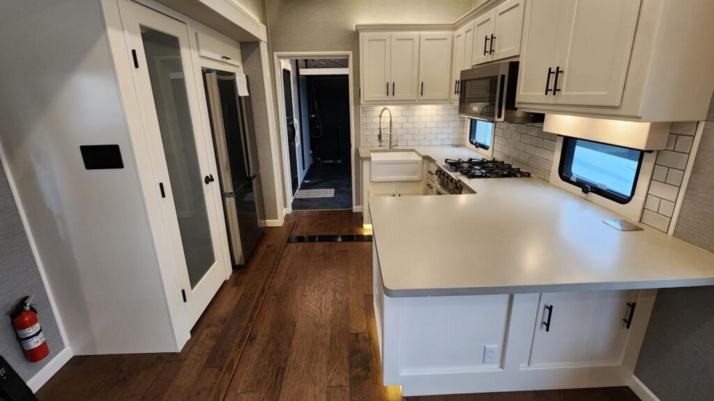 The kitchen in a new New Horizons RV showing all white cabinets and a door to the toy hauler portion. 