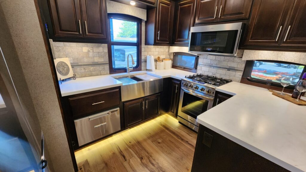A rear kitchen in a New Horizons RV fifth wheel, with white counters and dark brown cabinets.