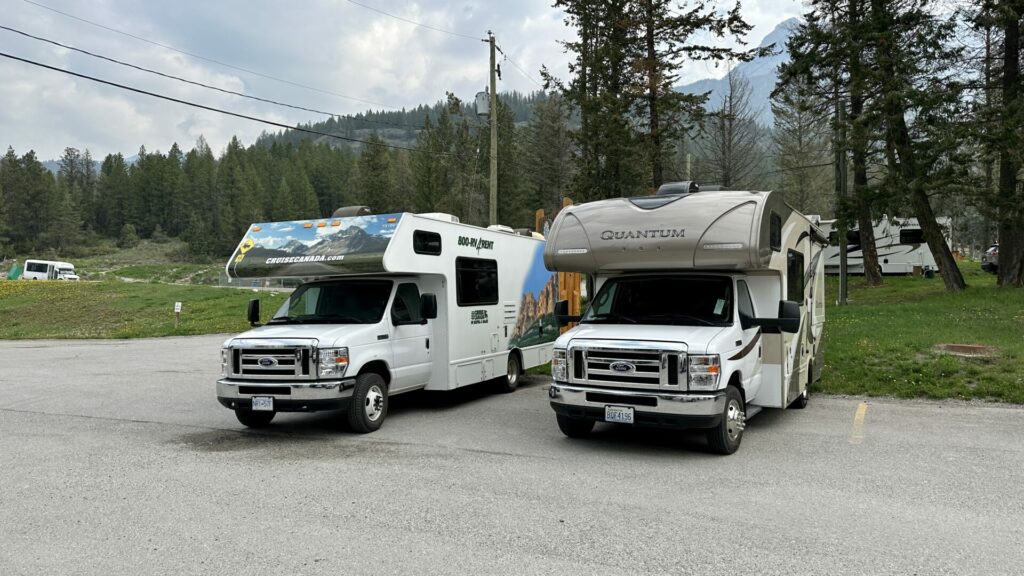 An RV rental parked next to another RV with mountains in the background. 