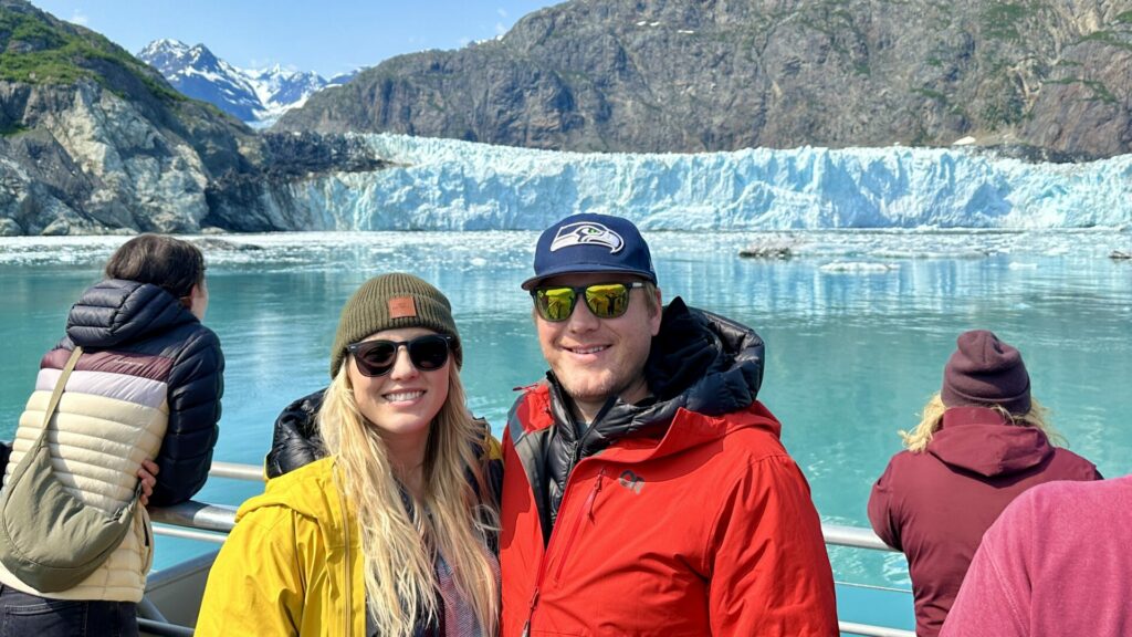 Jason and Rae standing on a boat smiling with a glacier in the background.
