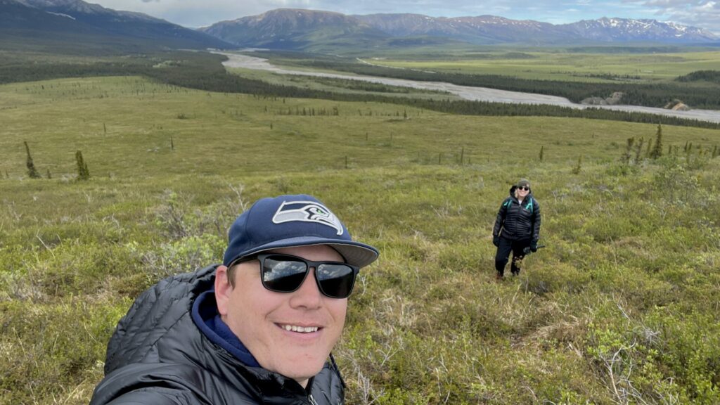 Jason taking a selfie with Rae in the background at Denali National Park on a sunny day.