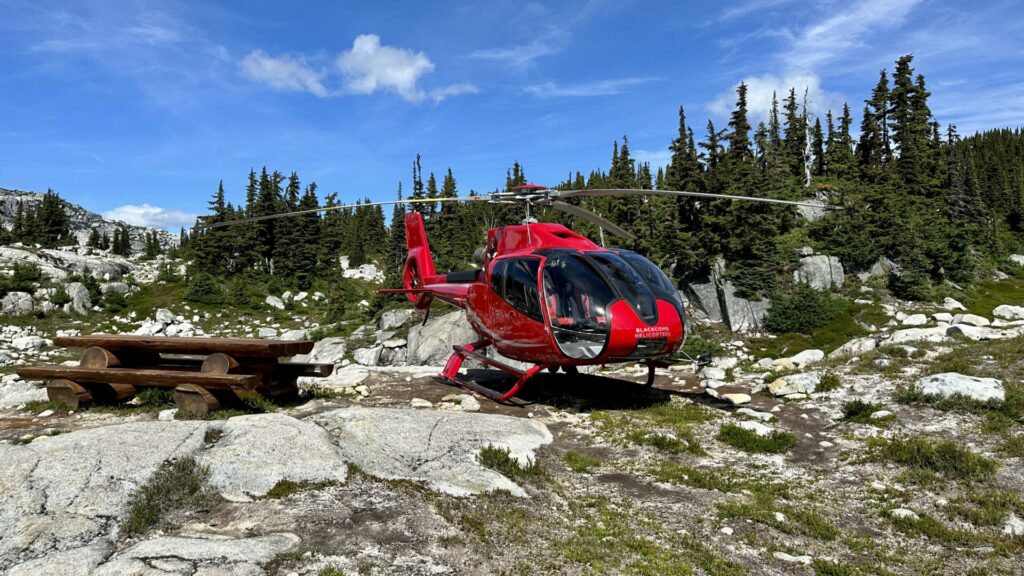 A red helicopter that landed next to a picnic table and an alpine lake. 