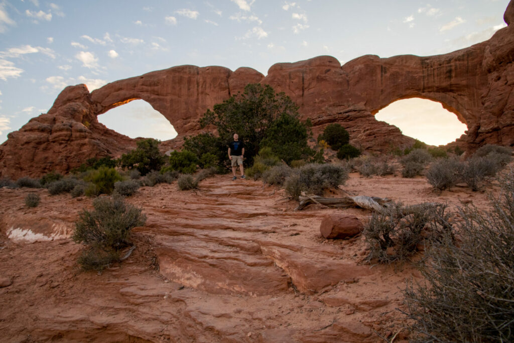 A man standing between Double Arch  at sunset.