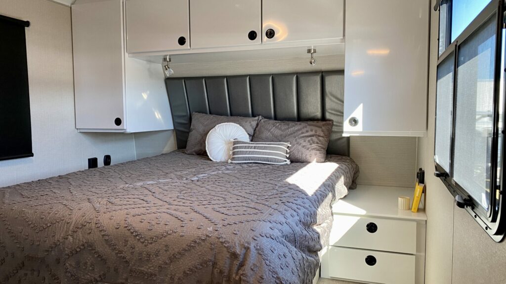 An RV mattress inside a travel trailer with white cabinets and a gray comforter.