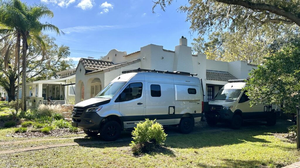 Two class B camper vans parked in a house's driveway on a sunny day.