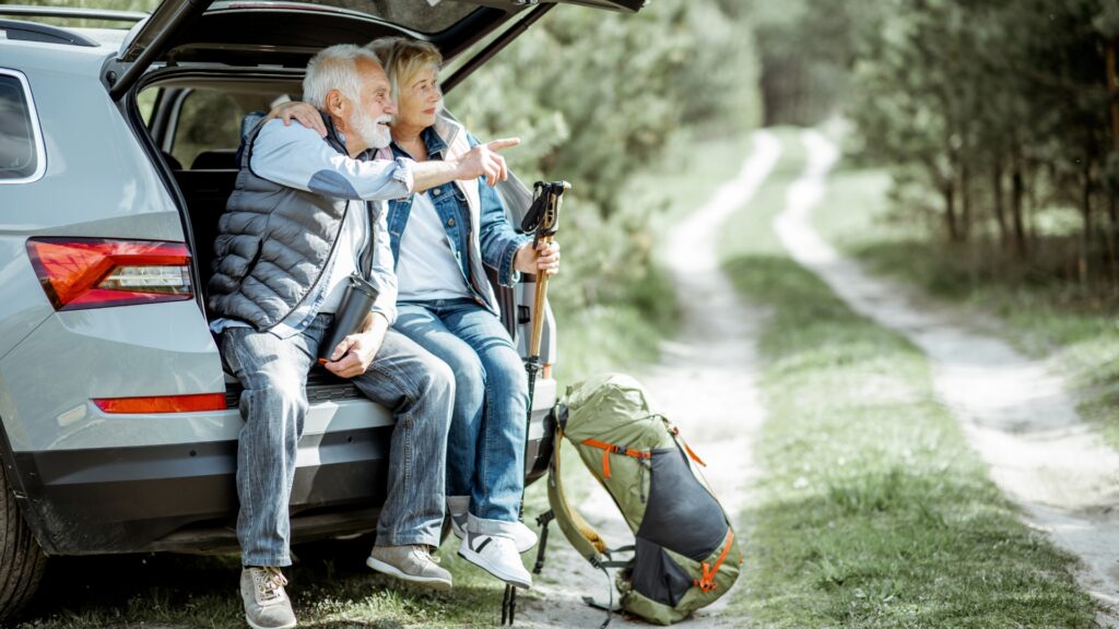 A senior couple sitting in the hatch back of their car with one of them pointing to the distance and the other holding hiking gear.