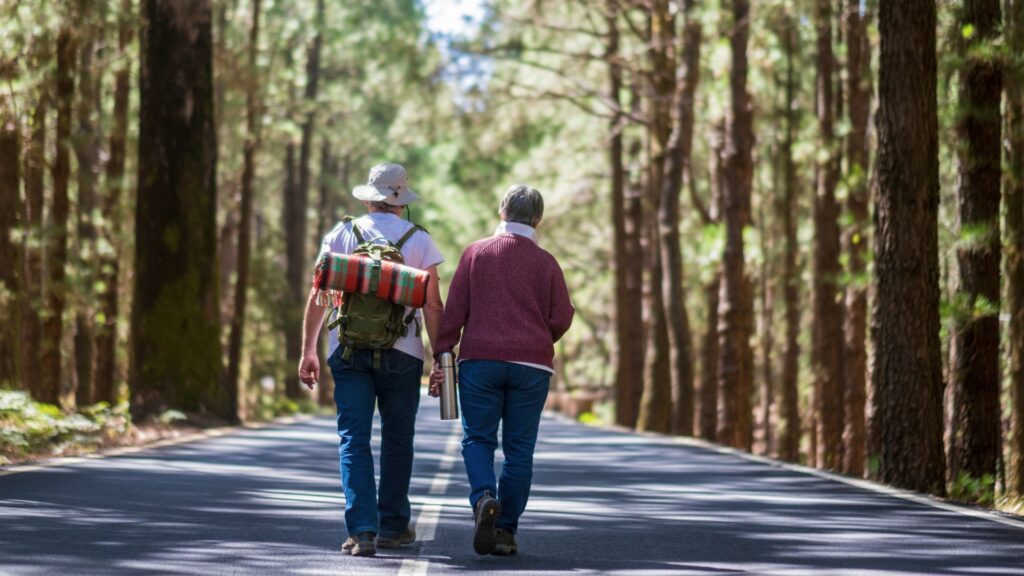 A senior couple walking down a paved road with tall trees lining it.