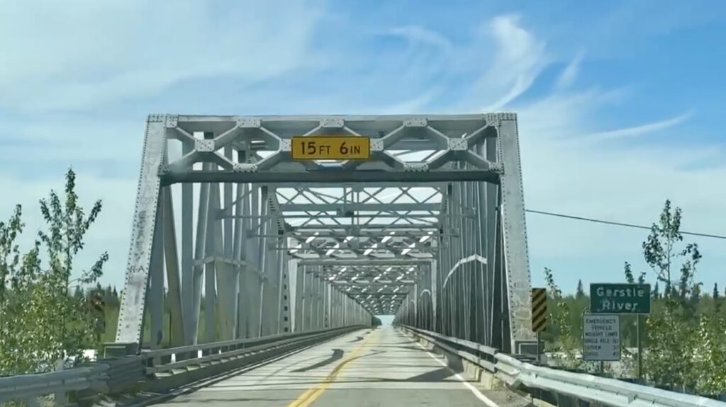 A bridge over a river with a yellow sign showing the height clearance is 15 feet 16 inches.