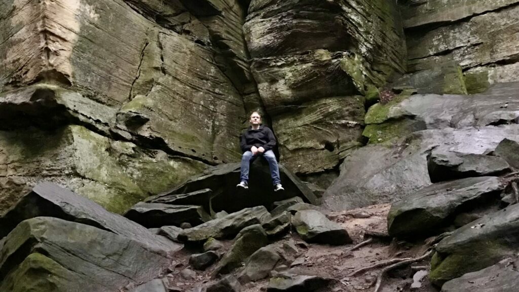 Jason sitting on a rock with steep broken rock sheets behind him in cuyahoga valley national park.