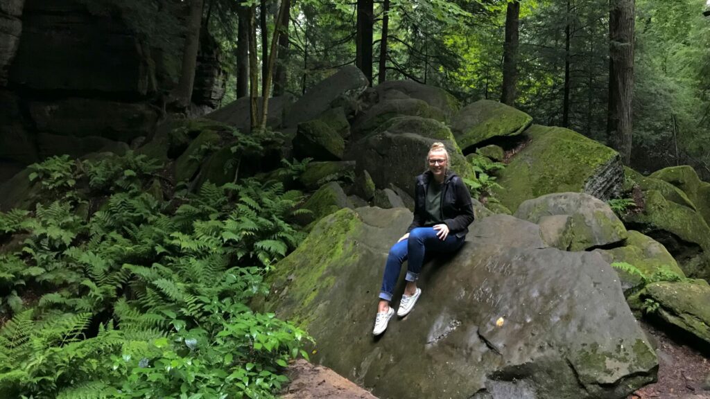 Rae sitting on a rock with lush green fern and trees on the background at cuyahoga valley national park. 