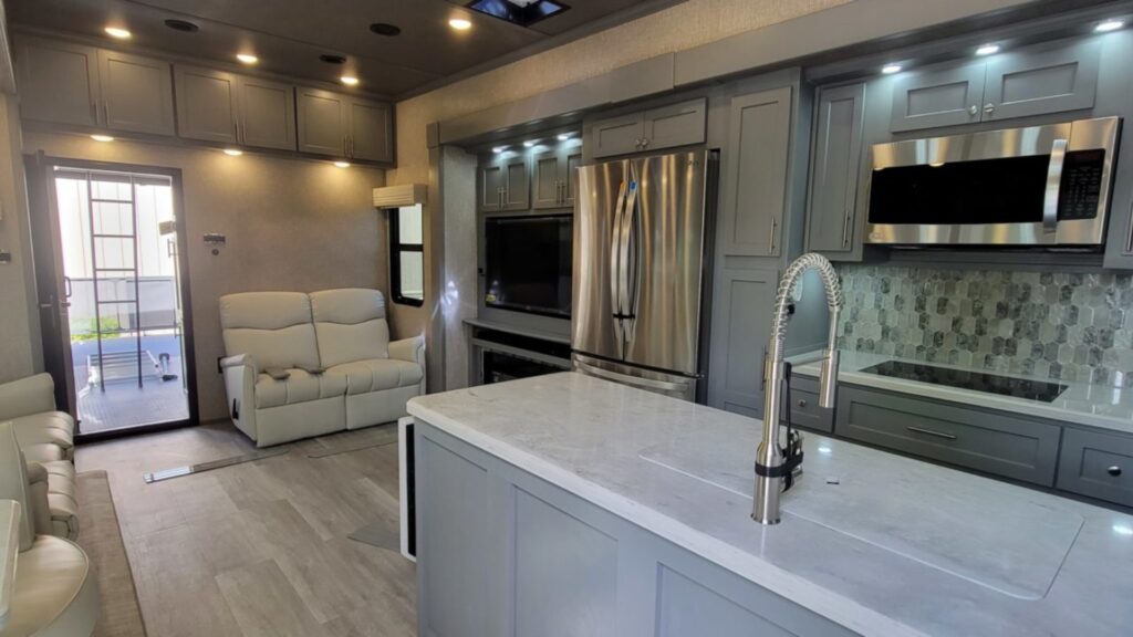 Interior shot of a Luxe toy hauler with a gray kitchen, large living room and the back door to the toy hauler section on the left.