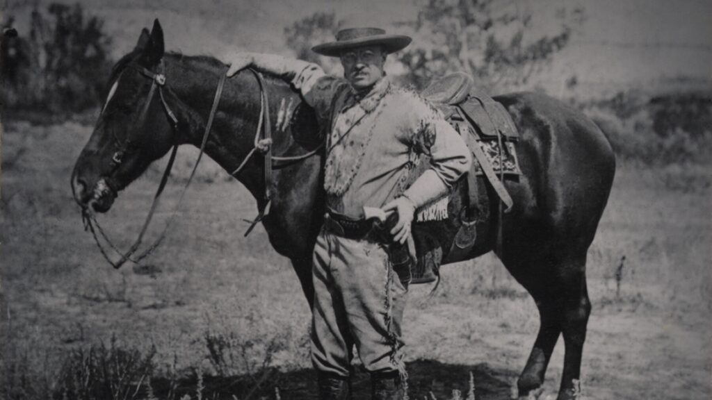 An old black and white photo of Theodore Roosevelt on his ranch in North Dakota with a horse. 