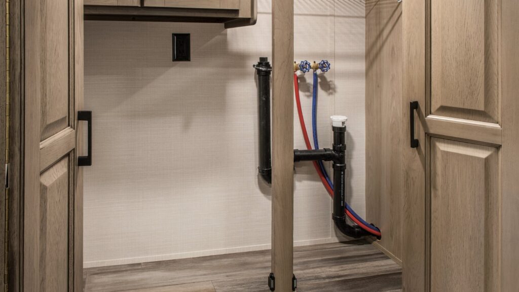 The interior of a cupboard in a DRV Mobile Suites fifth wheel that has the washer and dryer hookups.