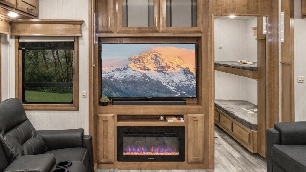 The interior of a DRV fifth wheel showing the TV in the living room and a door to the right of it that goes into a bunk room with a full bathroom.