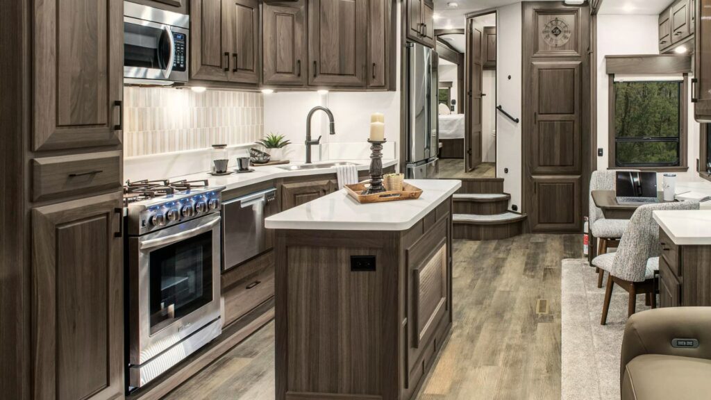 The interior of a DRV Mobile Suites fifth wheel showing brown cupboards and white countertops in the kitchen.