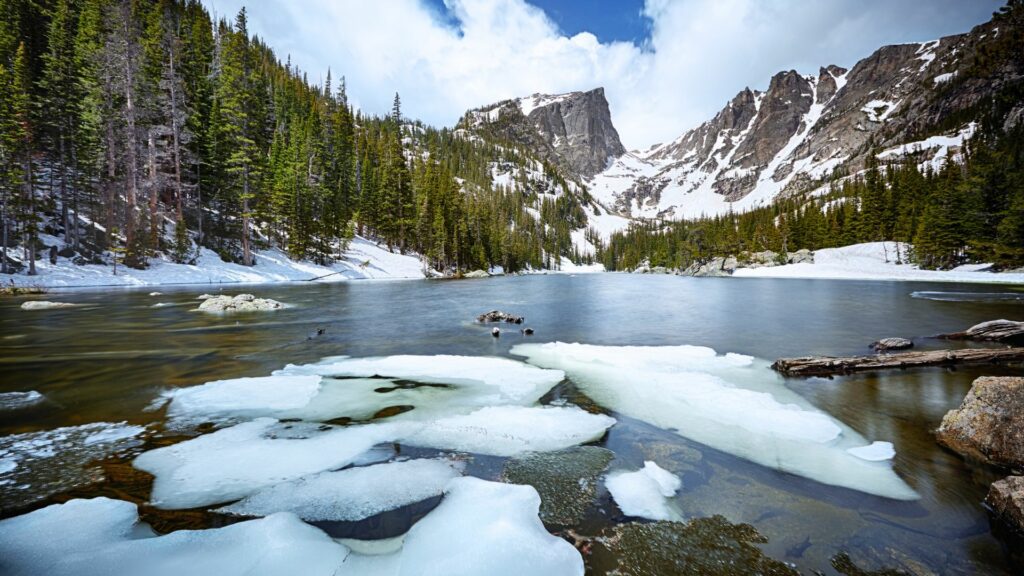 Dream Lake inside Rocky Mountain National Park with ice chunks still on the water surface and mountains in the background.