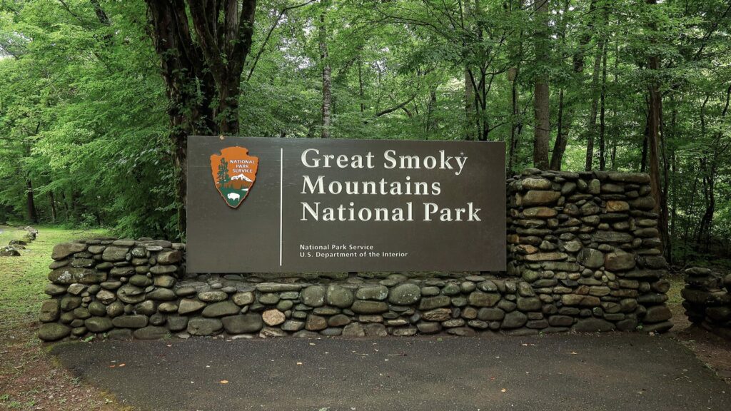 Greaty Smoky Mountians National Park Sign posted on a rock wall with the forest in the background.