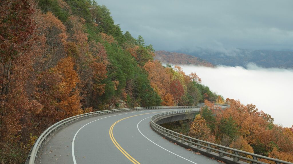 Road going through fall foliage covered mountains with fog in the backgound. 