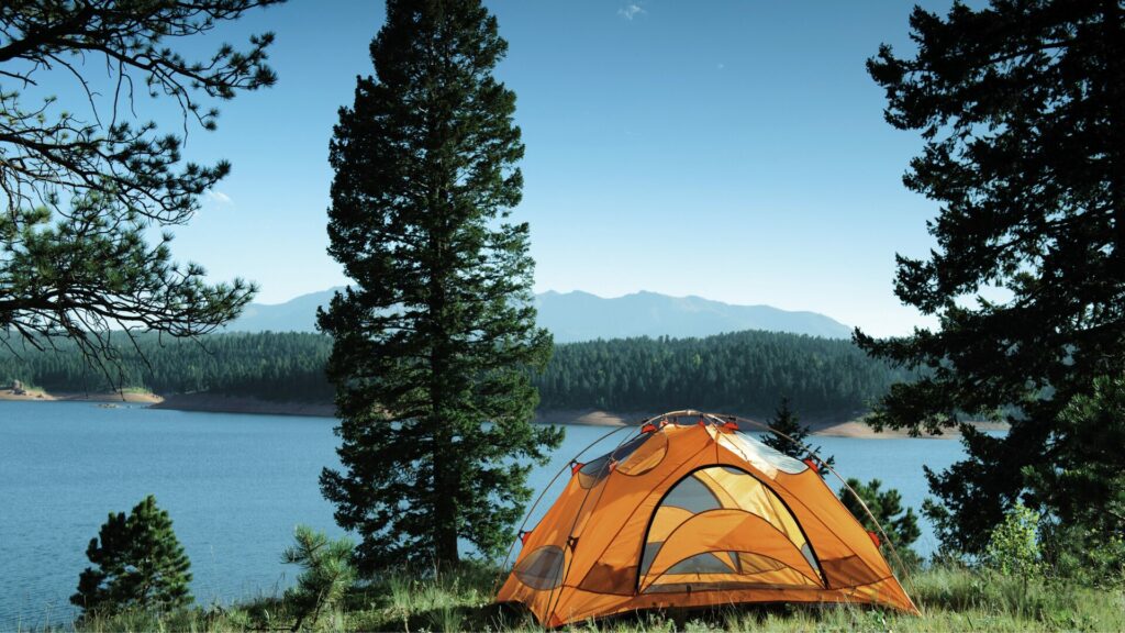 Orange camping tent outlooking over a body of water and a mountain range in the background.