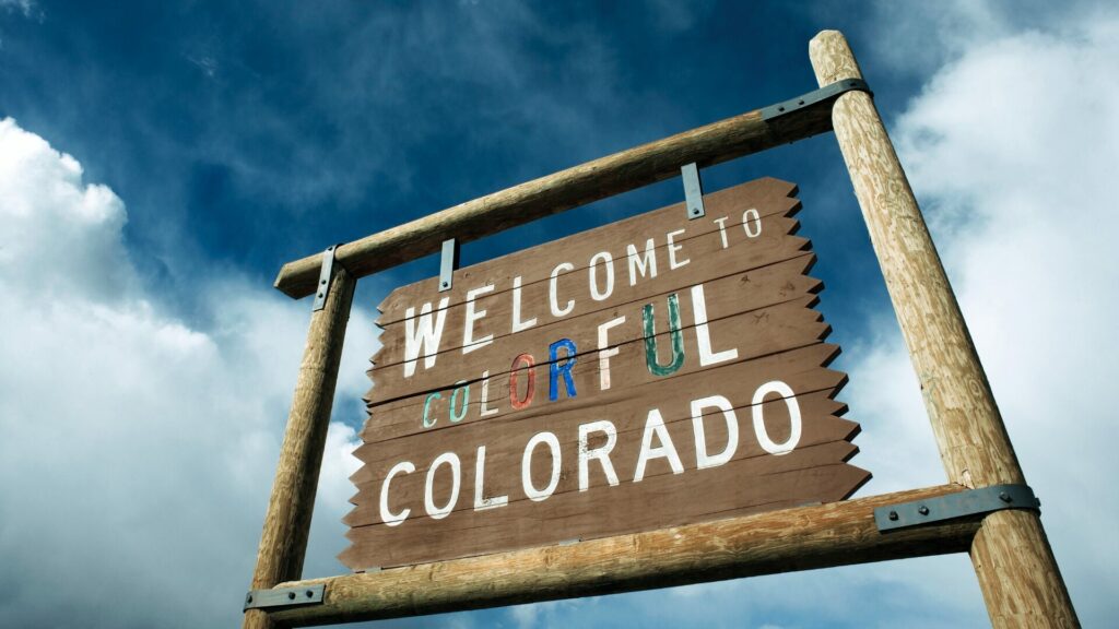 Wooden Welcom to Colorful Colorado sign with cloudy blue sky in the background. 