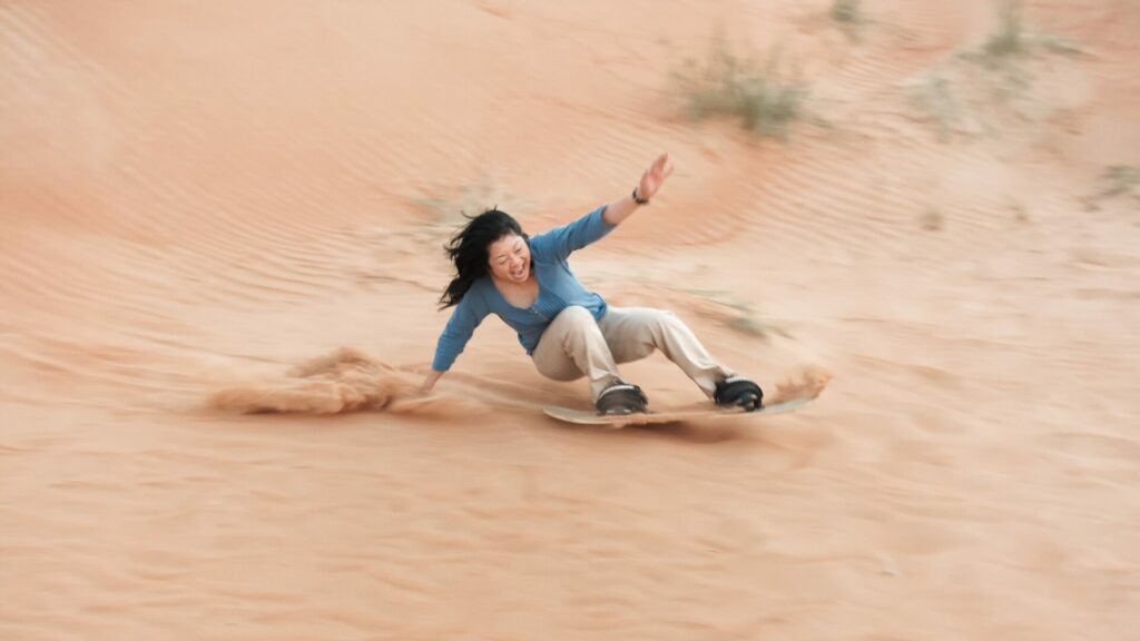 Woman sandboarding down a sand dune.