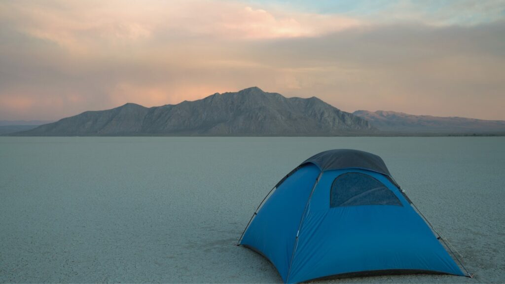 Blue tent camping in desert with mountain range in the background.