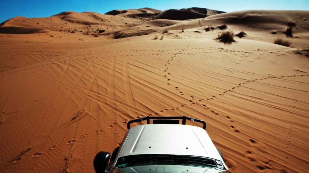 An aerial view of the hood of a truck in the remote desert with footsteps imprinted in the sand. 