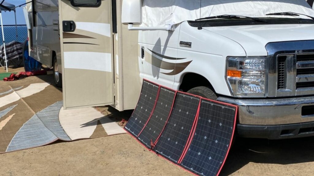 Four portable solar panels leaning up against an RV in the sun.