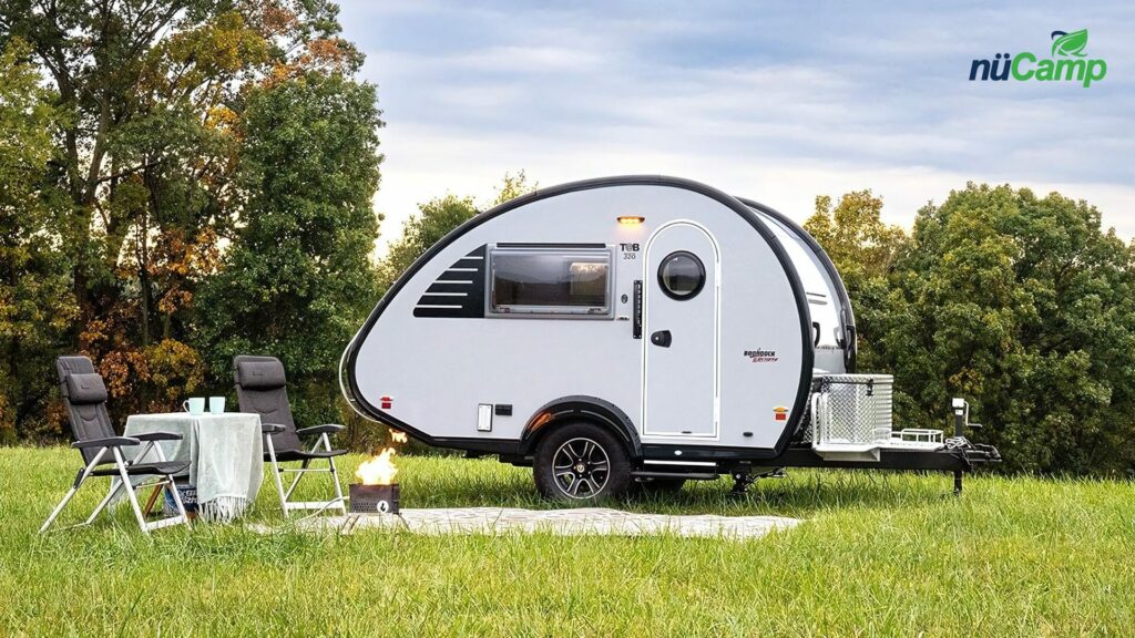 nuCamp Tab 320S in a field with an outdoor camp set up in front of it. 