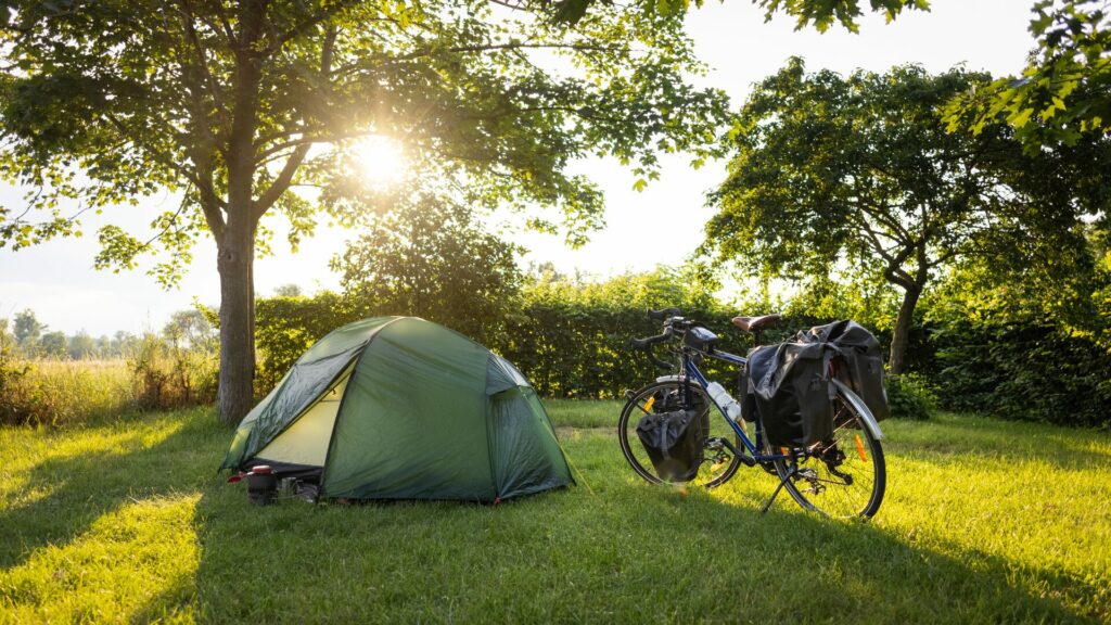 A bike standing next to a small green tent in the mddle of a grassy area with trees behind it. 