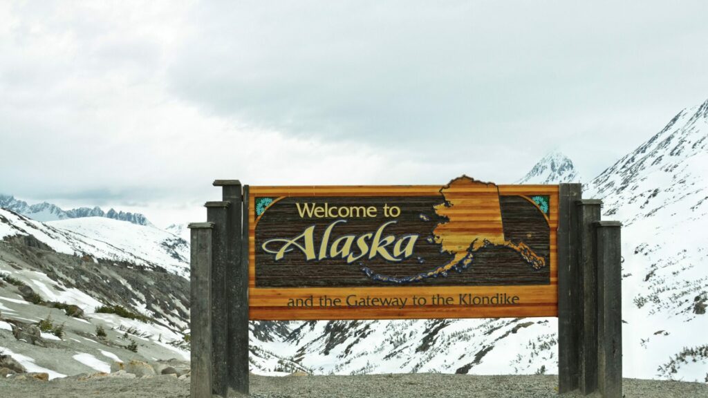 Welcome to Alaska Sign in front of snowy mountains. 