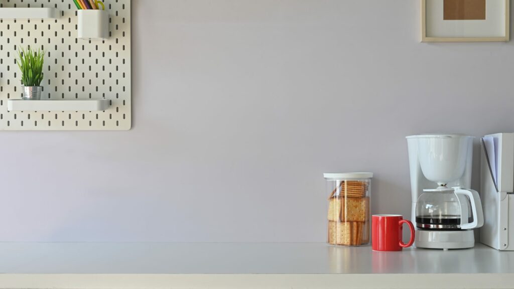 A small coffee bar with a red mug and some crackers in a container. 