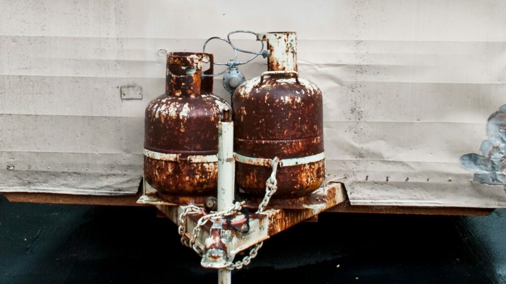 Two rusted propane tankes attached to the hitch of an RV trailer. 