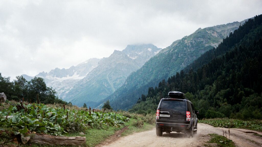 An SUV driving through some mountains on a dirt road. 