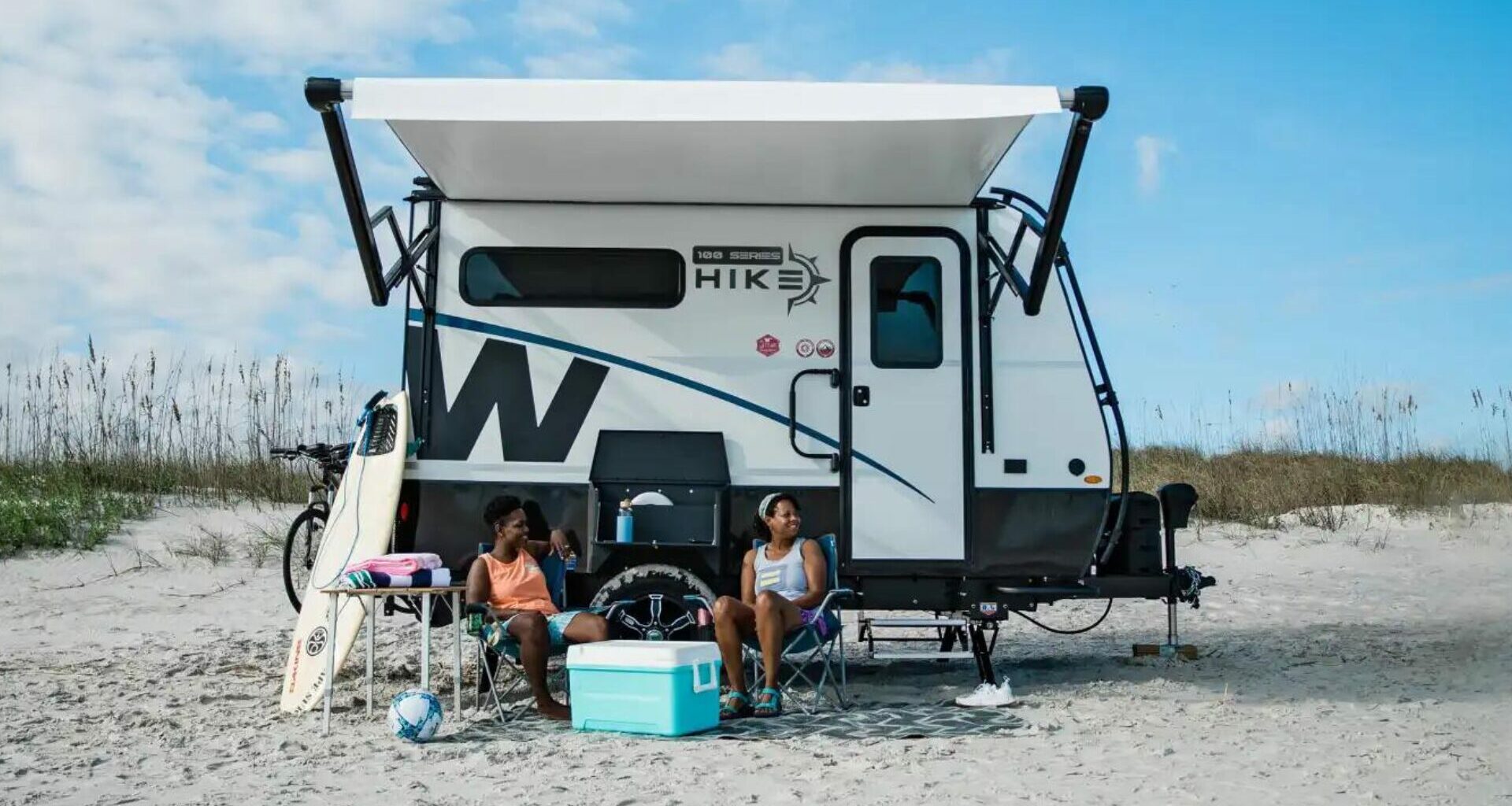 Two people sitting in front of their Winnebago Hike 100 on the beach.