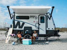 Two people sitting in front of their Winnebago Hike 100 on the beach.