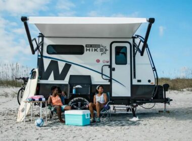 Two people sitting in front of their Winnebago Hike 100 on the beach.