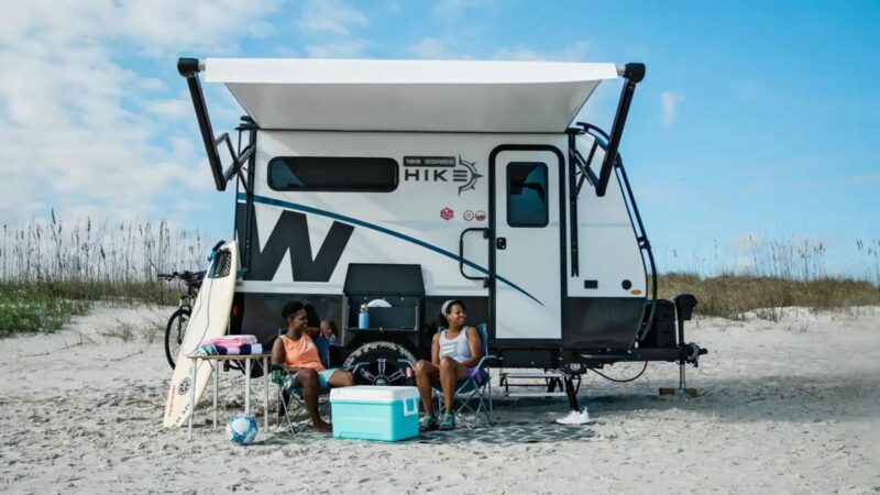 Two people sitting in front of their Winnebago Hike 100 on the beach.