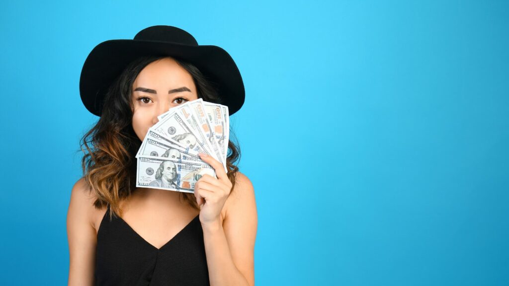 A woman holding up $800 in $100 bills with a blue background. 