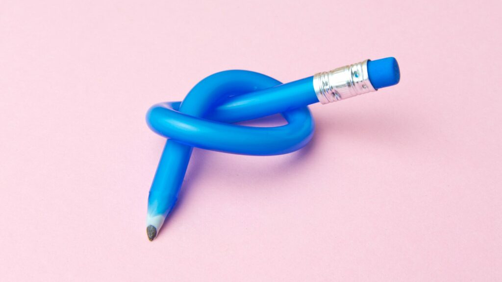 A blue flexible pencil tied into a knot on a light pink background. 