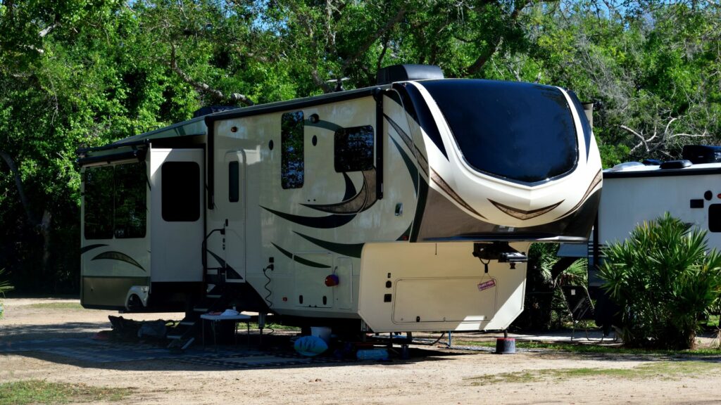 A fifth wheel RV with slideouts sitting in a lot with a densely forested background. 