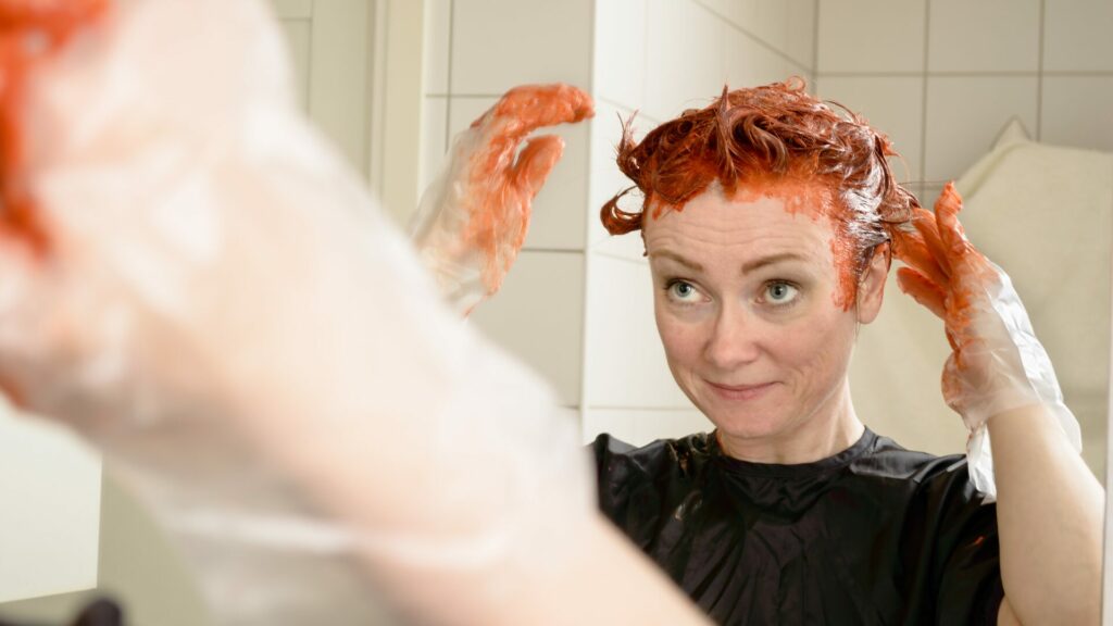 Woman in bathroom dying their hair bright orange. 