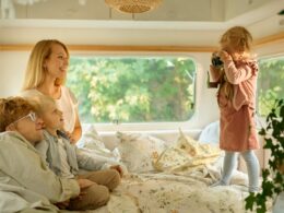 Family of four lounging on a bed in their RV.