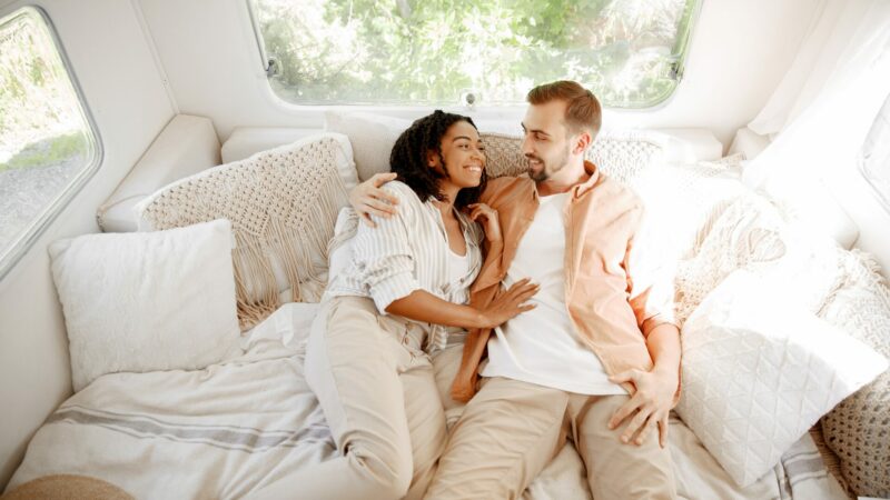 A couple in their RV bed as they look into each other's eyes smiling.