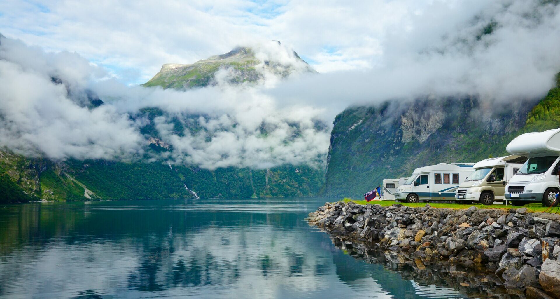 A row of motorhomes parked along an embankment of a turqoise lake and mountain range.